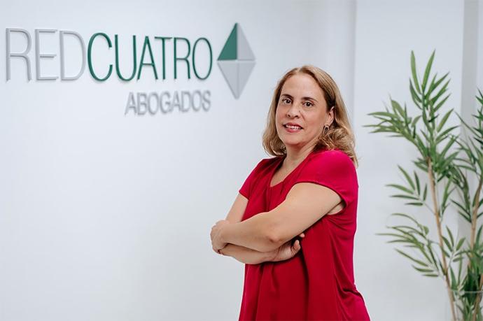 MARÍA DEL MAR ÁLVAREZ DORTA Abogada vestida de rojo posando delante de la pared del logo RedCuatro Abogados