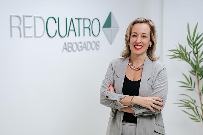 CAROLINA ROMÁN MONTOTO Abogada vestida de traje gris posando frente a pared con logo de RedCuatro Abogados